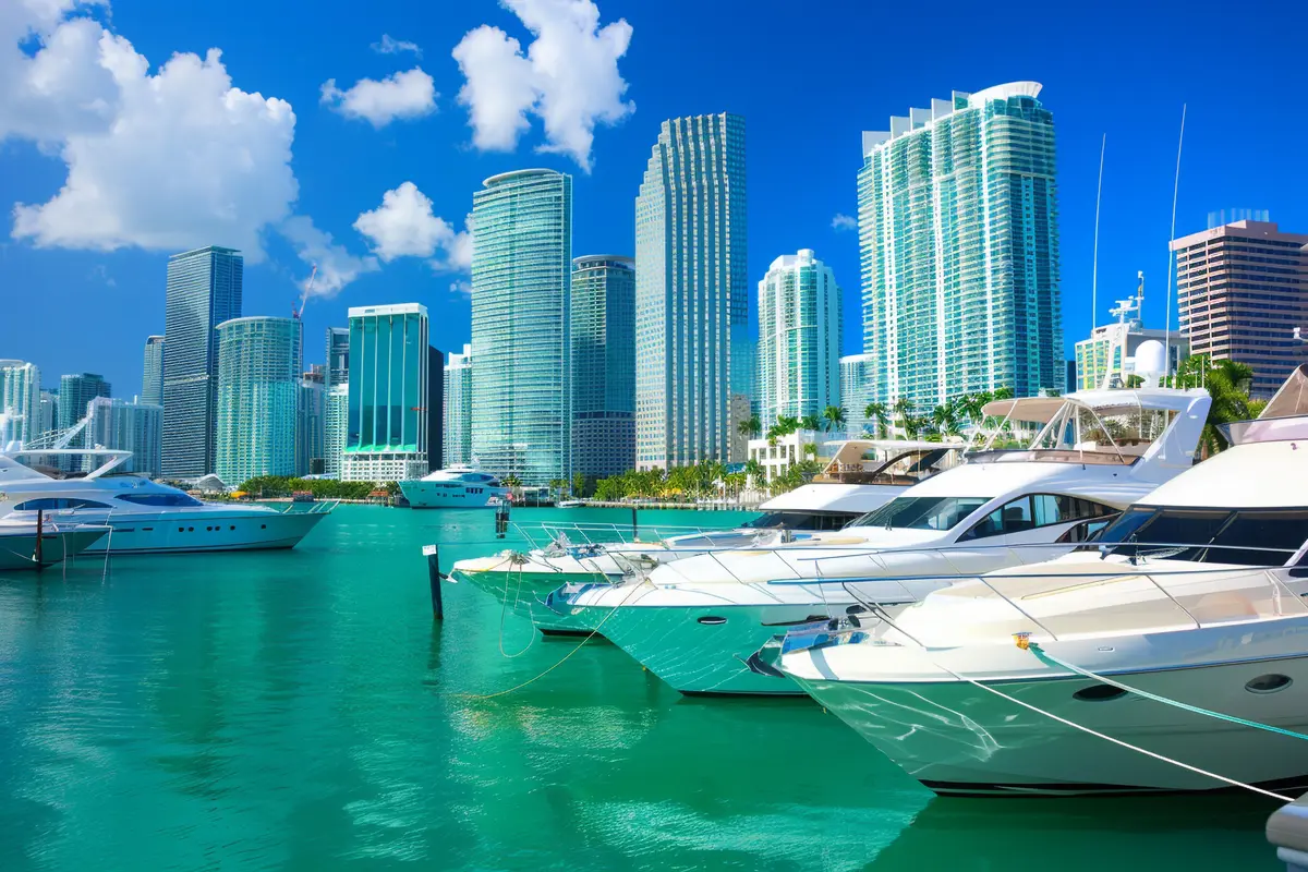 Iates de luxo ancorados na marina com os arranha-céus do Downtown de Miami ao fundo.