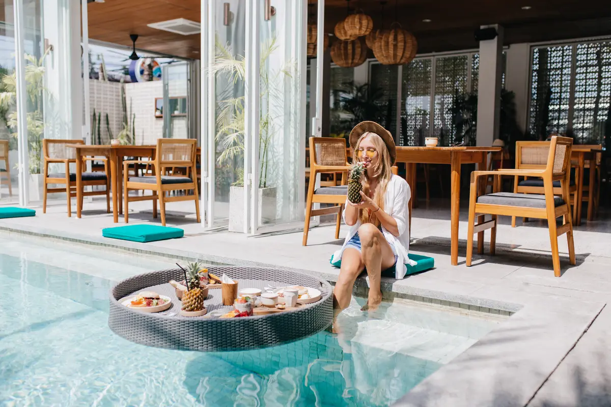 Woman relaxing by a pool with a floating breakfast tray at a luxury villa.