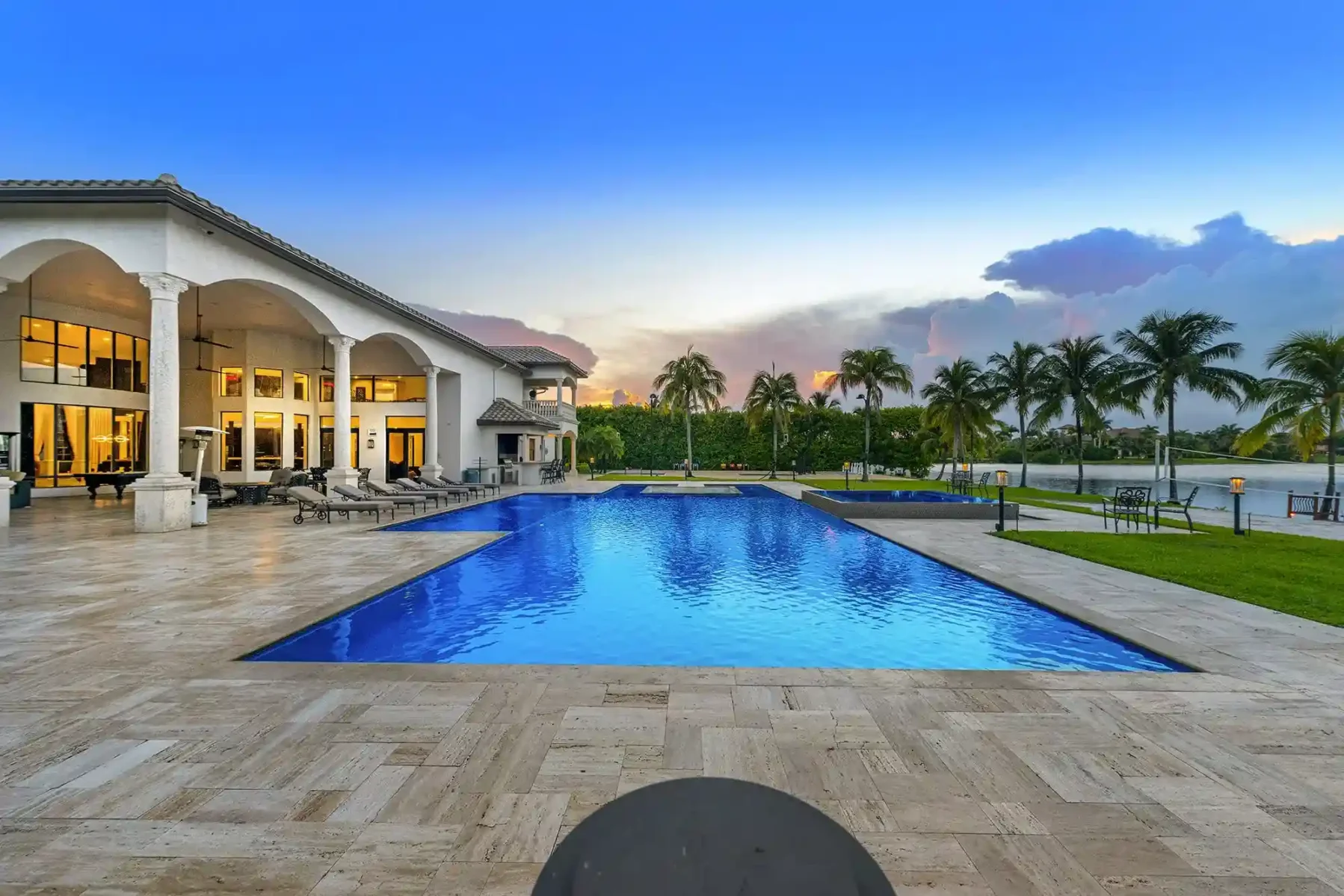 Mansão Villa Lova com piscina ampla, área de lazer e palmeiras ao pôr do sol.