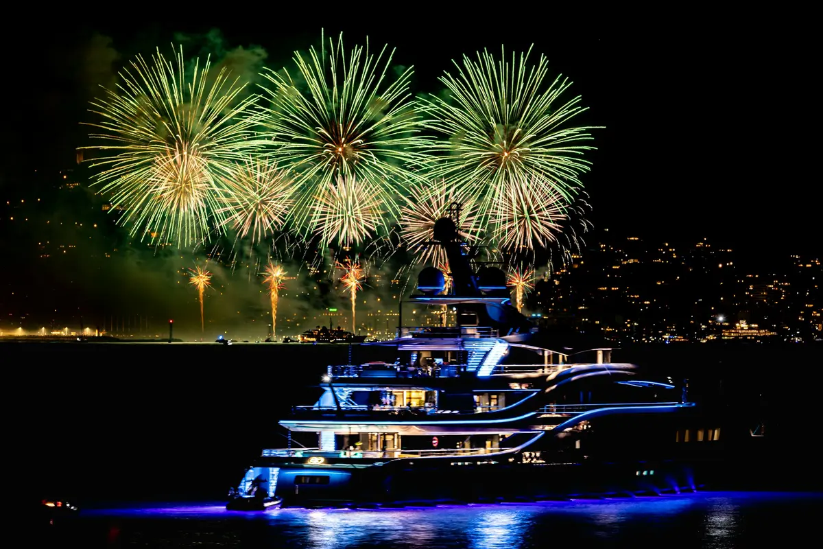 Yate de lujo iluminado con luces azules navegando durante los fuegos artificiales de Año Nuevo en Miami.